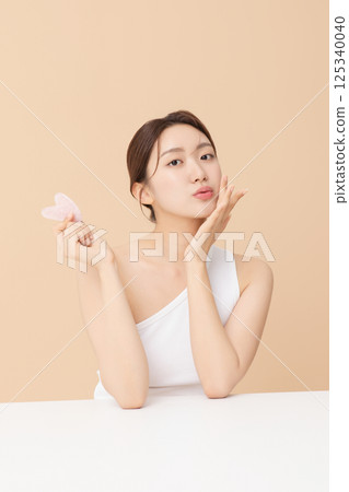Portrait of a young woman massaging her skin using gua sha 125340040