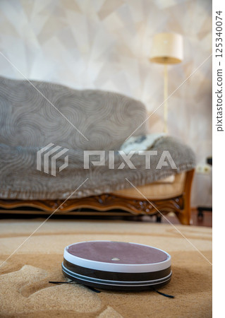Robot vacuum autonomously cleaning a carpet at home. Concept of smart cleaning technology and automated home maintenance. 125340074