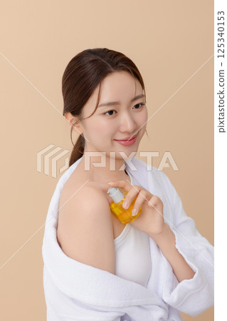Cropped view of young woman wearing robe and applying oil to skin after shower 125340153