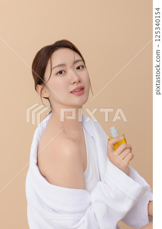Cropped view of young woman wearing robe and applying oil to skin after shower 125340154