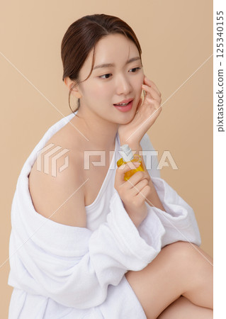 Cropped view of young woman wearing robe and applying oil to skin after shower 125340155