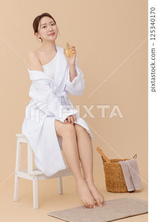 Cropped view of young woman wearing robe and applying oil to skin after shower 125340170