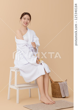 Cropped view of young woman wearing robe and applying oil to skin after shower 125340184