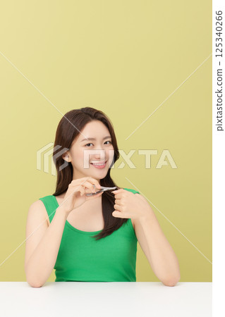 Cropped view of young woman taking care of her nails with nail clippers 125340266