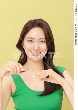 Cropped view of young woman taking care of her nails with nail clippers 125340277