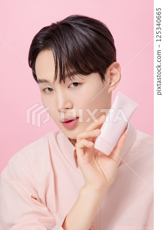 Portrait of a young man posing while holding a tube product Portrait of a young man posing while holding a tube product 125340665