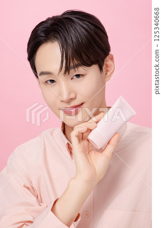 Portrait of a young man posing while holding a tube product Portrait of a young man posing while holding a tube product 125340668