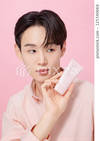 Portrait of a young man posing while holding a tube product Portrait of a young man posing while holding a tube product 125340669