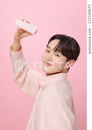Portrait of a young man posing while holding a tube product 125340675