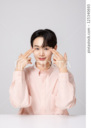 Portrait of a young man smiling while touching his face with his hands 125340693