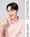 Portrait of a young man smiling while touching his face with his hands 125340756
