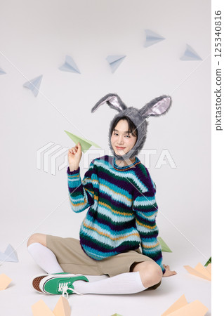 Cropped view of young man wearing bunny hat sitting surrounded by paper airplanes 125340816