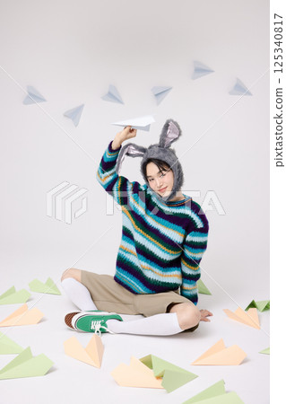 Cropped view of young man wearing bunny hat sitting surrounded by paper airplanes 125340817