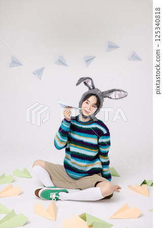 Cropped view of young man wearing bunny hat sitting surrounded by paper airplanes 125340818