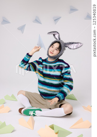 Cropped view of young man wearing bunny hat sitting surrounded by paper airplanes 125340819