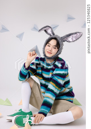 Cropped view of young man wearing bunny hat sitting surrounded by paper airplanes 125340825