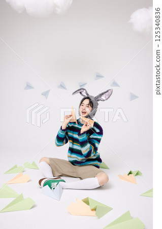 Cropped view of young man wearing bunny hat sitting surrounded by paper airplanes 125340836