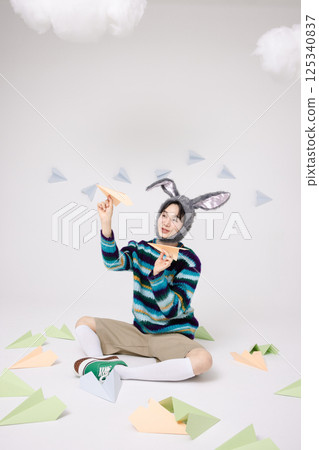 Cropped view of young man wearing bunny hat sitting surrounded by paper airplanes 125340837