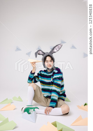 Cropped view of young man wearing bunny hat sitting surrounded by paper airplanes Cropped view of young man wearing bunny hat sitting surrounded by paper airplanes 125340838