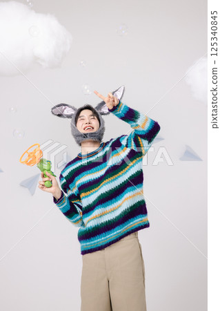 Portrait of a man standing wearing a rabbit hat and holding soap bubbles 125340845