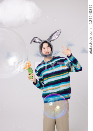 Portrait of a man standing wearing a rabbit hat and holding soap bubbles 125340852