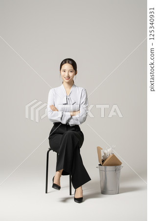 A neat-looking young woman in her 20s sitting on a chair next to a trash can containing drugs and syringes 125340931