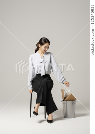A neat-looking young woman in her 20s sitting on a chair next to a trash can containing drugs and syringes A neat-looking young woman in her 20s sitting on a chair next to a trash can containing drugs and syringes 125340935