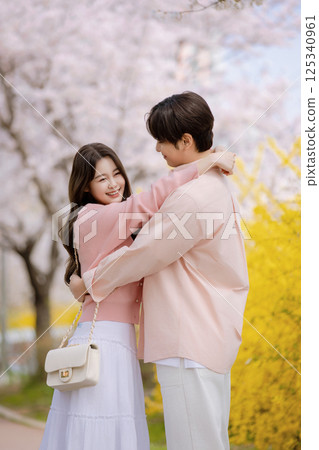 A friendly couple enjoying a date on a street filled with cherry blossoms 125340961