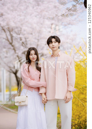 A friendly couple enjoying a date on a street filled with cherry blossoms 125340962