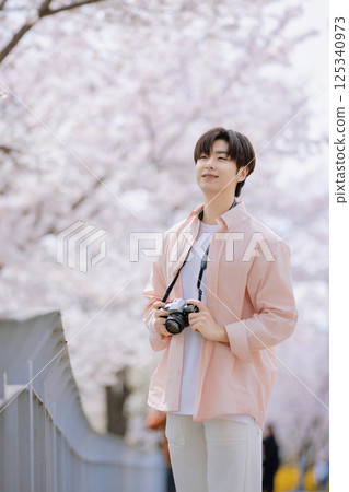 Portrait of a young man photographing cherry blossoms with a camera 125340973