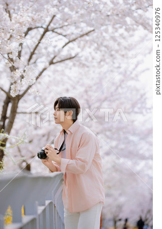 Portrait of a young man photographing cherry blossoms with a camera Portrait of a young man photographing cherry blossoms with a camera 125340976