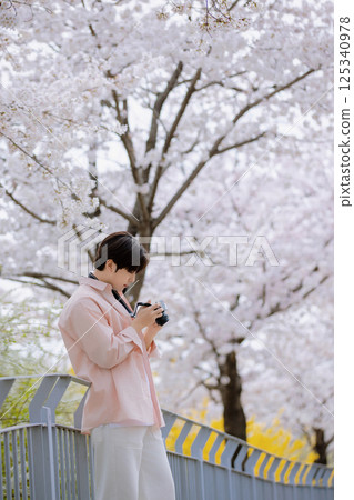 Portrait of a young man photographing cherry blossoms with a camera 125340978