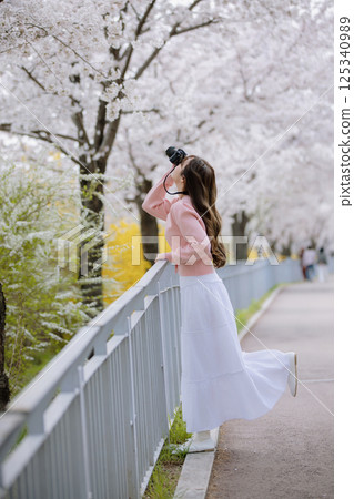 Portrait of a young woman photographing cherry blossoms with a camera 125340989