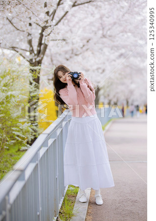 Portrait of a young woman photographing cherry blossoms with a camera 125340995