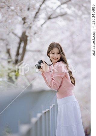 Portrait of a young woman photographing cherry blossoms with a camera 125340999