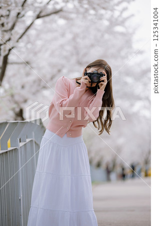 Portrait of a young woman photographing cherry blossoms with a camera Portrait of a young woman photographing cherry blossoms with a camera 125341004