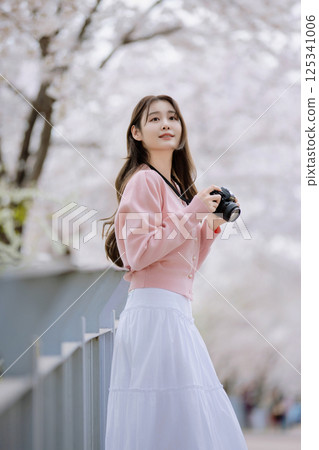 Portrait of a young woman photographing cherry blossoms with a camera 125341006