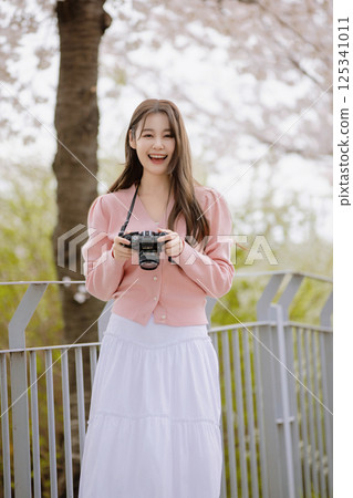 Portrait of a young woman photographing cherry blossoms with a camera 125341011