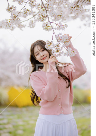 A lovely woman holding a cherry blossom and taking a picture 125341095
