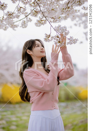 A lovely woman holding a cherry blossom and taking a picture A lovely woman holding a cherry blossom and taking a picture 125341096