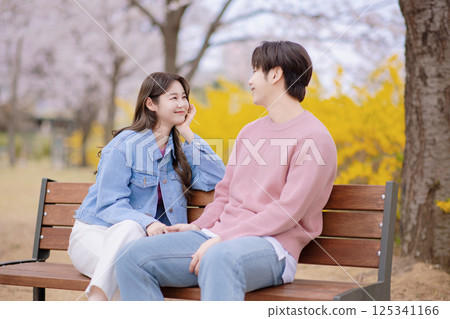 A couple enjoying a date on a park bench with flowers in full bloom 125341166