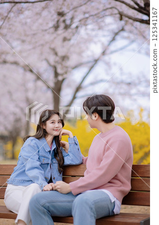A couple enjoying a date on a park bench with flowers in full bloom A couple enjoying a date on a park bench with flowers in full bloom 125341167