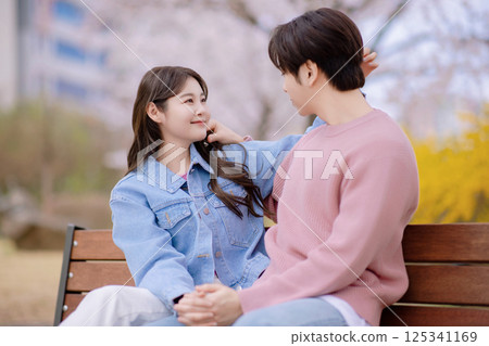 A couple enjoying a date on a park bench with flowers in full bloom A couple enjoying a date on a park bench with flowers in full bloom 125341169
