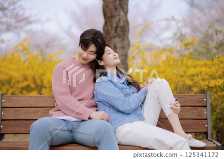 A couple enjoying a date on a park bench with flowers in full bloom 125341172