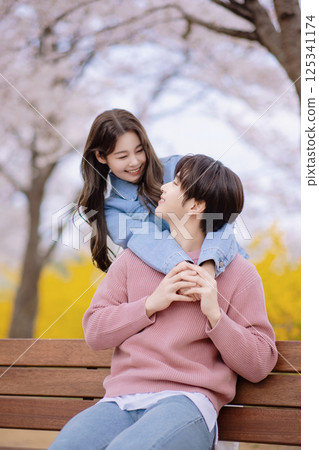 A couple enjoying a date on a park bench with flowers in full bloom A couple enjoying a date on a park bench with flowers in full bloom 125341174