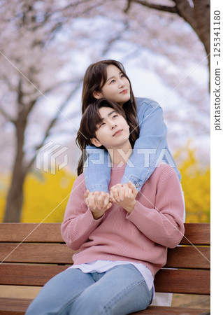 A couple enjoying a date on a park bench with flowers in full bloom 125341180