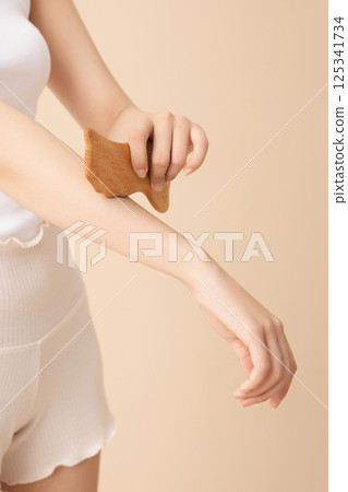 A woman massaging her arms with gua sha A woman massaging her arms with gua sha 125341734