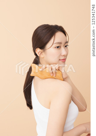 Portrait of a young woman massaging her shoulders with a gua sha 125341748