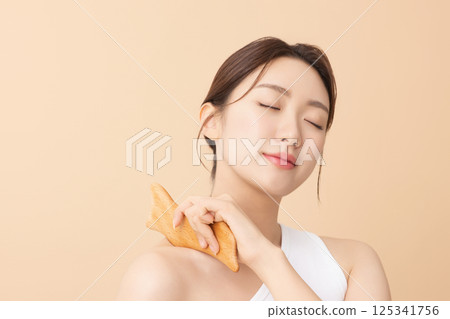 Portrait of a young woman massaging her shoulders with a gua sha 125341756