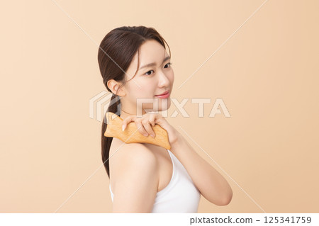 Portrait of a young woman massaging her shoulders with a gua sha 125341759